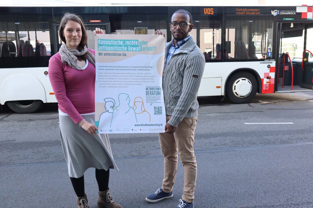 Sara Josef und Ambachew Anjulo von Exil präsentieren das Plakat der Betroffenenberatung Niedersachsen vor einem Bus der Stadtwerke Osnabrück