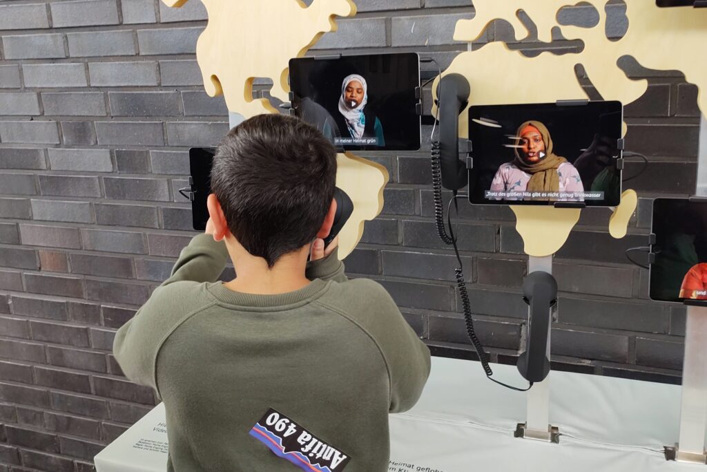 Junge schaut Videos in Ausstellung Fluchtgrund Klimawandel an
